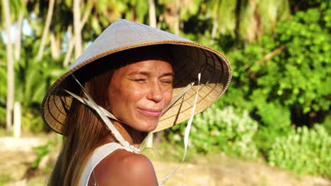 cute woman with conical hat in tropical forest smiles against sunshine, close up view