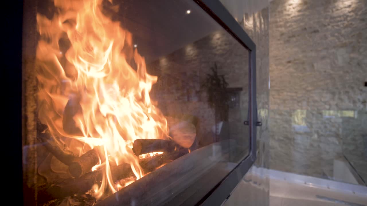 Luxury home fireplace with raging flames behind a glass case panel, Dolly out shot