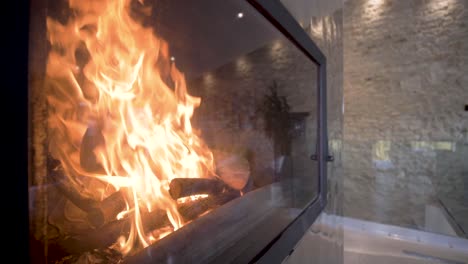 luxury home fireplace with raging flames behind a glass case panel, dolly out shot