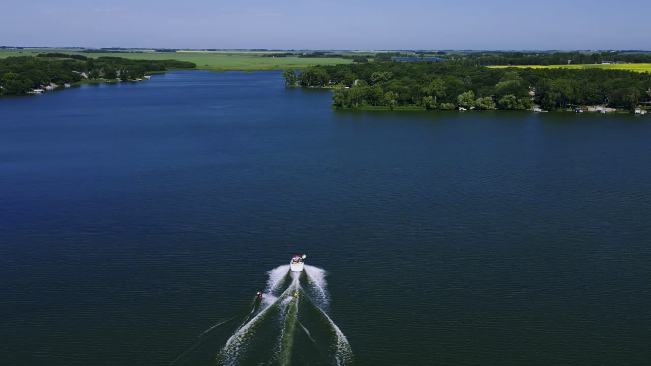 un avión no tripulado sigue a un barco de velocidad familiar que arrastra a dos wakeboarders en el lago killarney en turtle mountain, suroeste de manitoba, canadá.