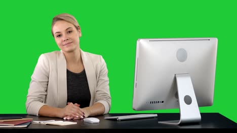 cheerful businesswoman sitting at the table in office and looking at camera on a green screen, chroma key