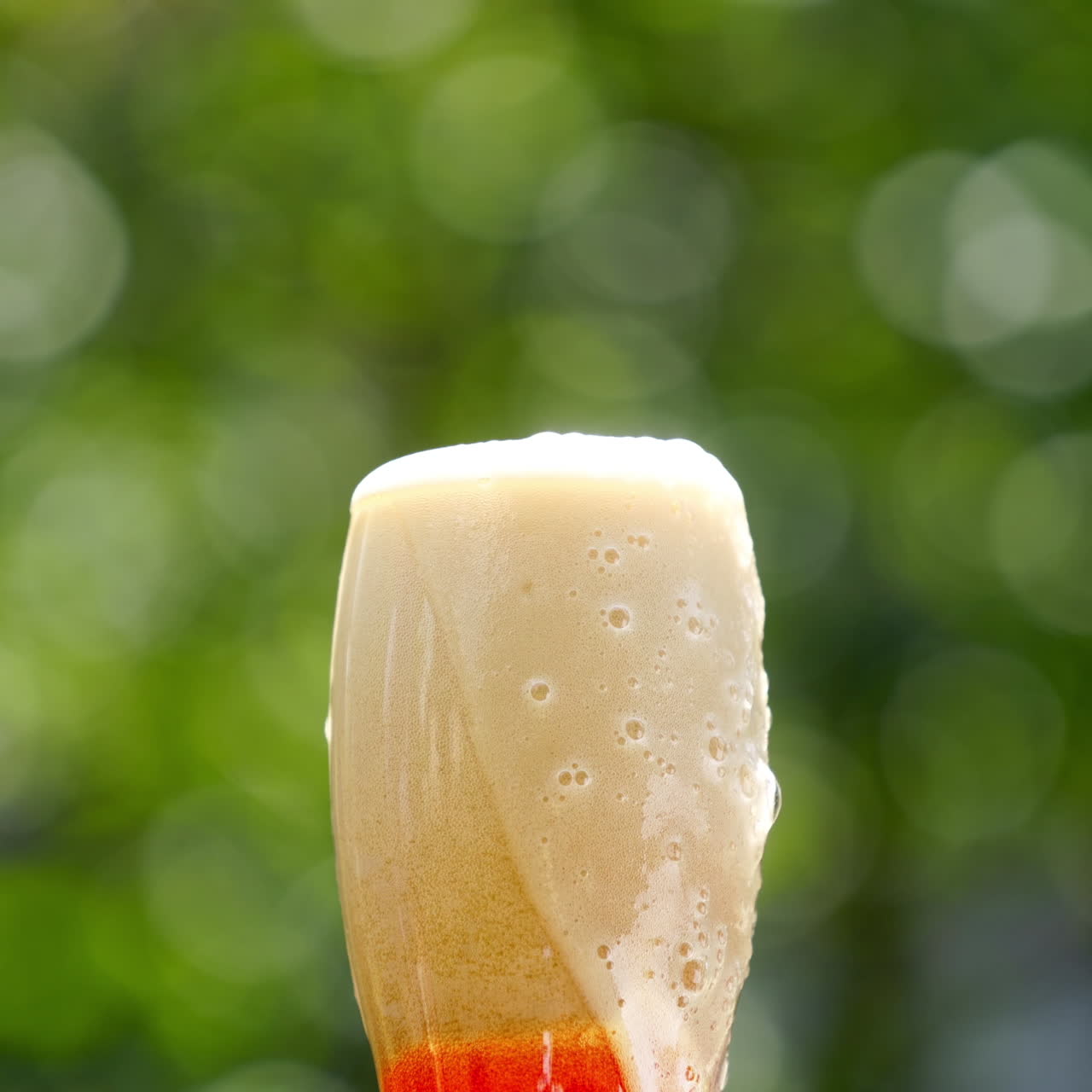Pouring fresh beer with foam running down. Stream of beer pours into a beer glass against blur green background. Close-up.