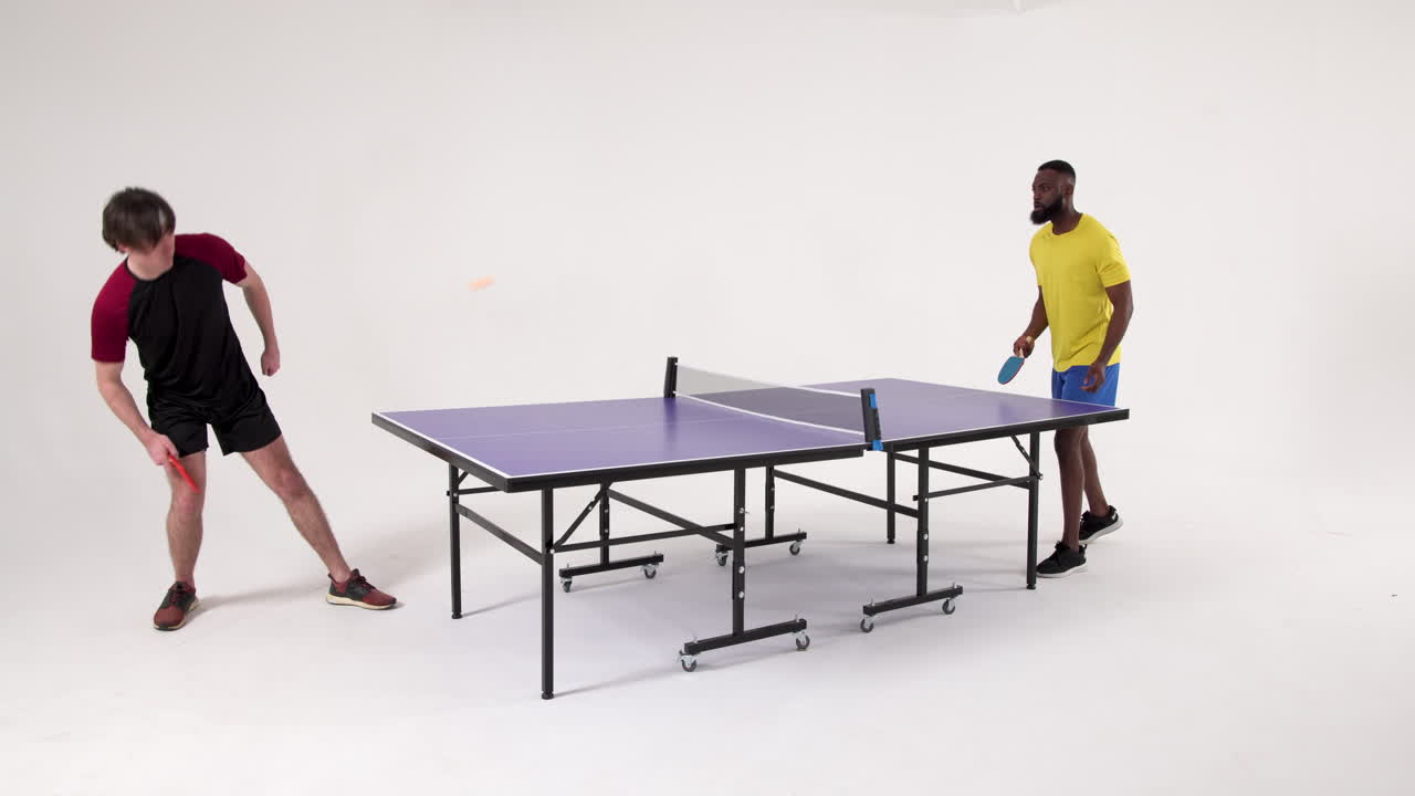 Playing table tennis, two men competing in match in studio setting