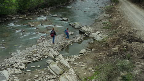 Excursionistas-Cruzando-El-Río-Vista-De-Drones-Nublado-Día-De-Primavera-Buscando-Vacaciones-De-Aventura