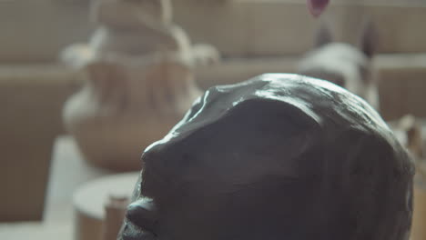 sculptor shaping face on clay head with wet hand