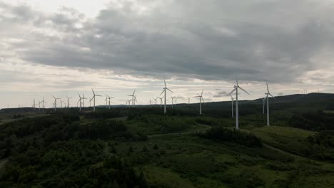 incredible spinning wind turbines produce green renewable energy above grass and tree covered hills on a cloudy day