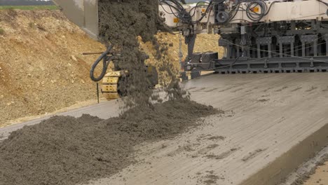 the excavator unloads fresh concrete onto the first layer of the formed road surface