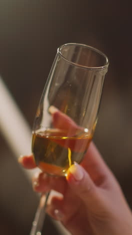 woman hand swirls wineglass of alcoholic drink enjoying pleasure of drinking in dimly lit hotel room overlooking nightlife. harm of alcohol on health and female alcoholism