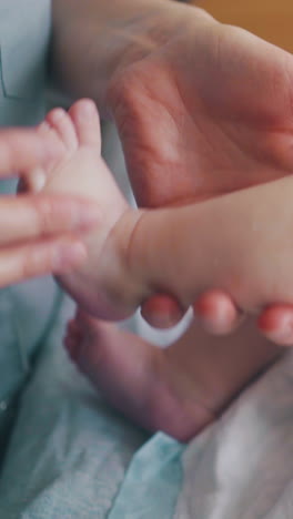 careful and skilled nurse holds infant boy leg lying on changing table and practices massage close view