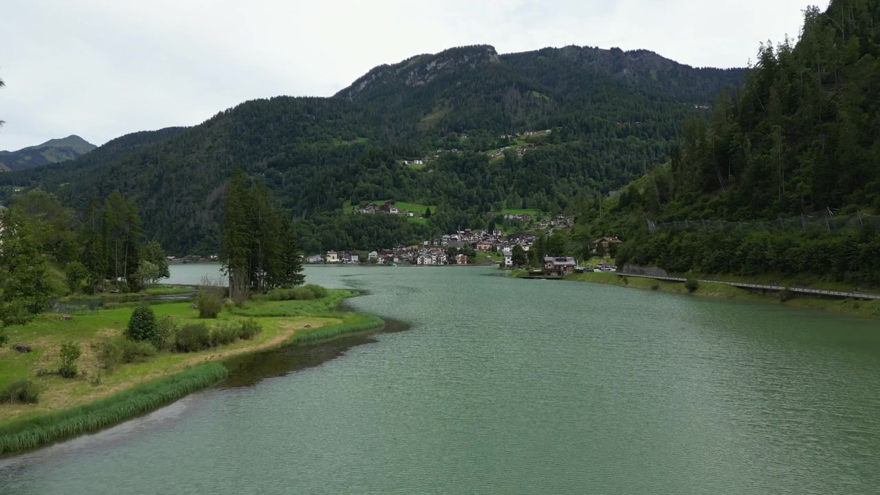 Splendide riprese con drone che sorvolano le tranquille acque verdi del Lago di Alleghe, rivelando l'incantevole villaggio di montagna incastonato nelle Alpi.