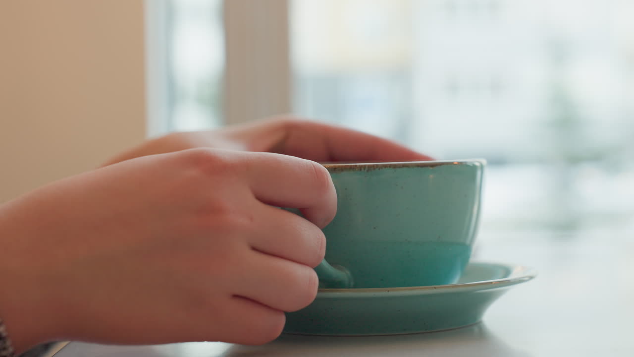 Gentle young woman in mall carefully places her cup of tea on table while watching cars pass through the window, creating a serene ambiance in the bustling city environment