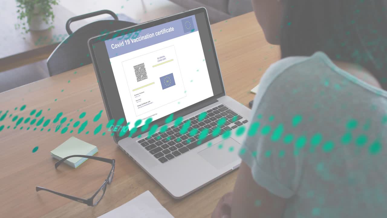 Man sitting reviewing Covid-19 certificate while scanning overlays verifying details across laptop