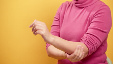 cerrar las manos de las mujeres aplicando crema en la piel de las manos y frotando los dedos y el brazo con un fondo amarillo