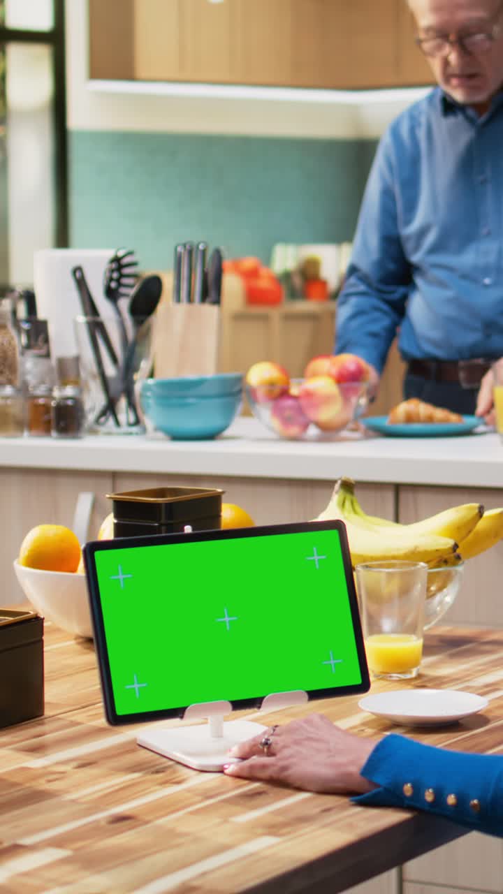 Vertical Video Green screen tablet with senior woman sitting at kitchen table with coffee cups