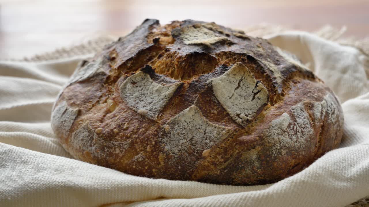 4K-Seitwärtsaufnahme von selbstgemachtem Sauerteigbrot, das sich auf Leinen von links nach rechts bewegt. Rustikales Artisan-Filmmaterial, ideal für Bäckerei- und kulinarische Themen.