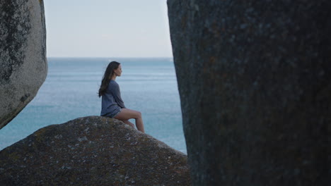 slow motion young beautiful woman tourist looking at ocean enjoying peaceful view of seaside wind blowing hair sitting on rock relaxing vacation