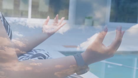 Animation-of-clouds-over-caucasian-woman-practicing-yoga-in-garden