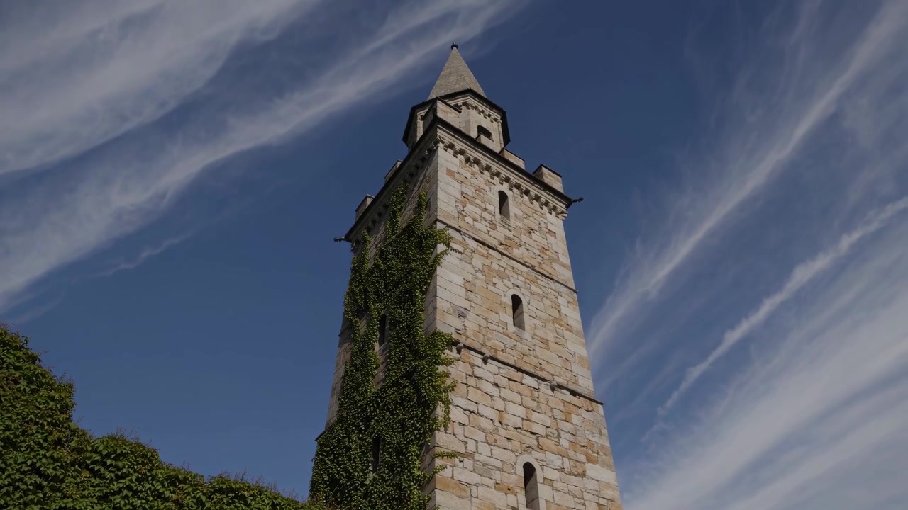 Lapso de tiempo de una antigua torre de piedra con hiedra contra un cielo azul