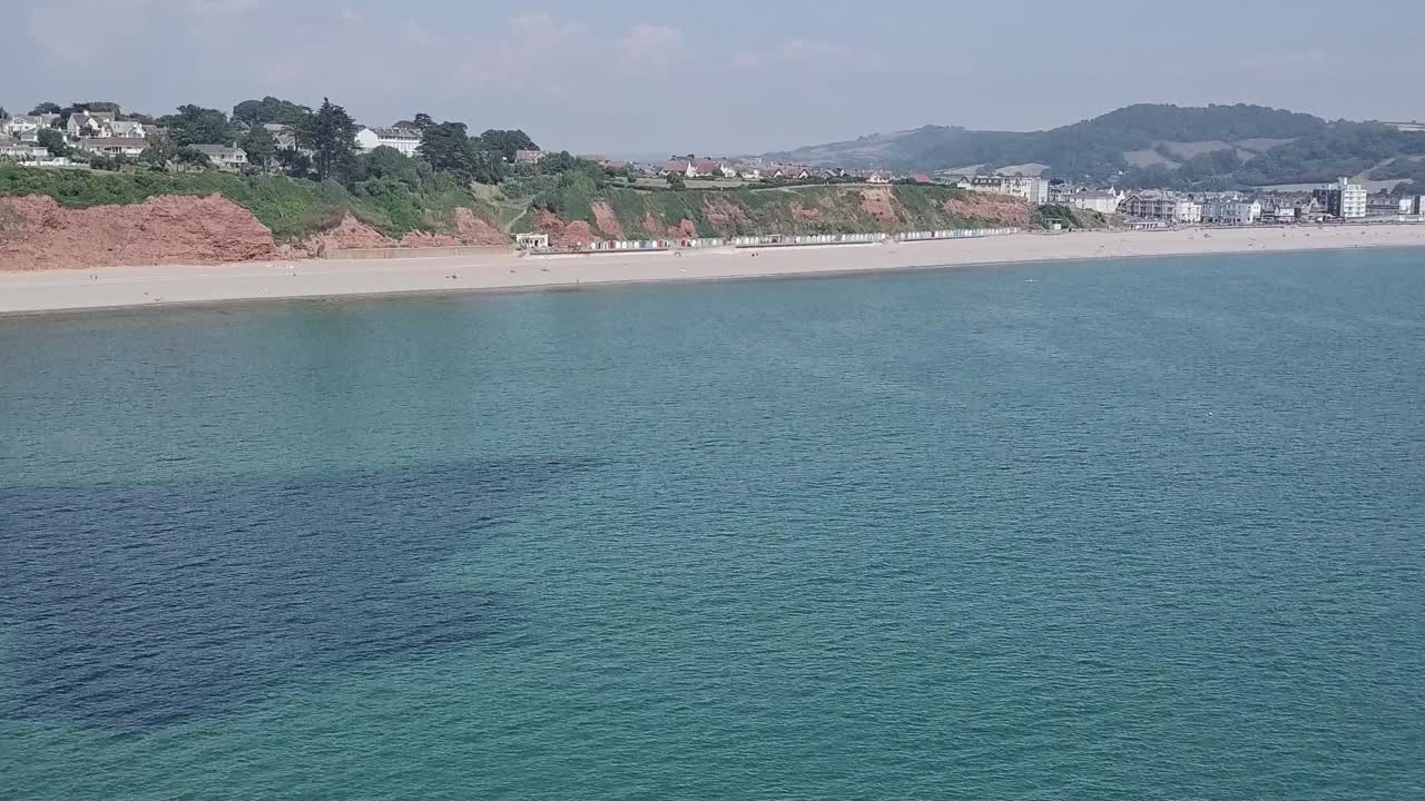 산 꼭대기에 집이 있는 리조트와 마을을 보여주는 영국 시턴의 쥐라기 해안선을 따라 드론이 이동합니다.