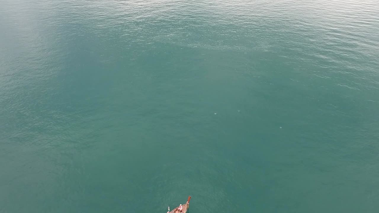 Drone footage of longtail boat navigating around islands of Krabi, Thailand with the limestone rock formations sticking out of the water and the ocean in background-1