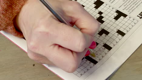 An-adult-woman-fills-out-an-answer-on-a-crossword-puzzle-with-a-black-pen