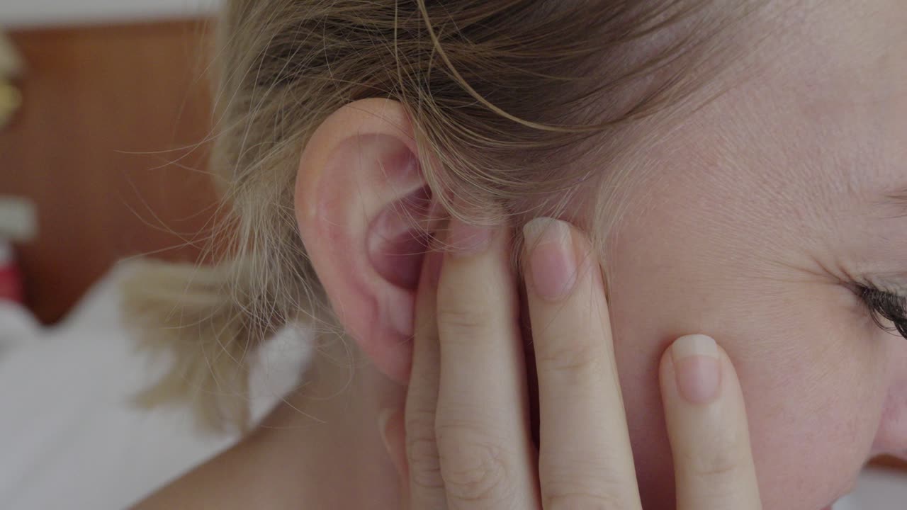 Close-up of a woman holding her ear and showing discomfort. The gesture and facial tension indicate earache, infection, or hearing problems in a medical context