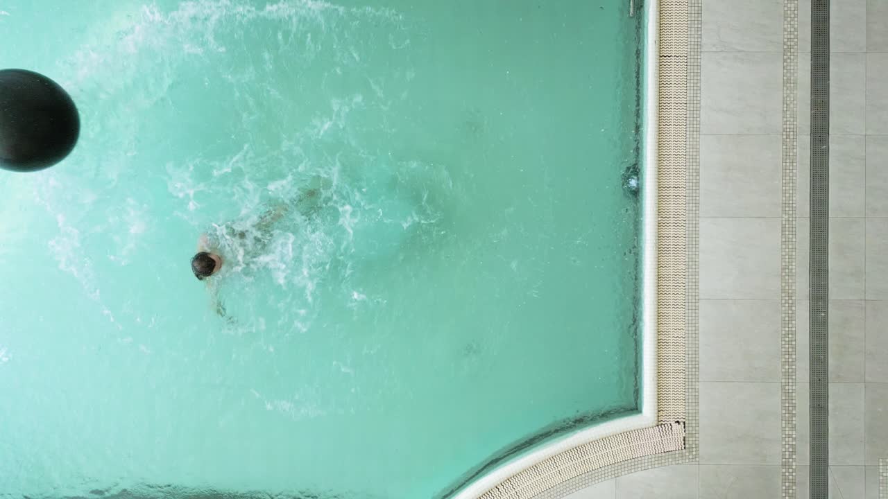 Overhead view of a person in a swimming pool with an inflatable ball and inner tube
