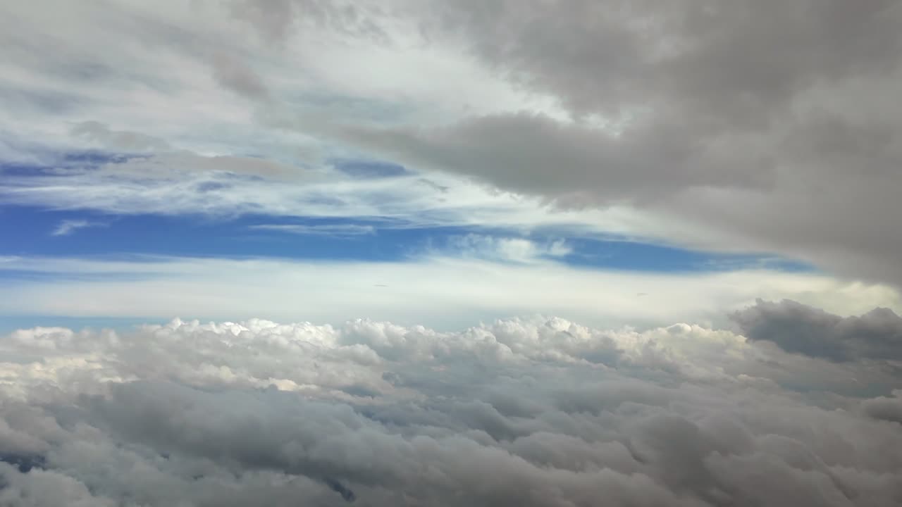 A high-altitude shot taken from a jet cockpit while flying between layers of ethereal clouds with a blue sky at the back.