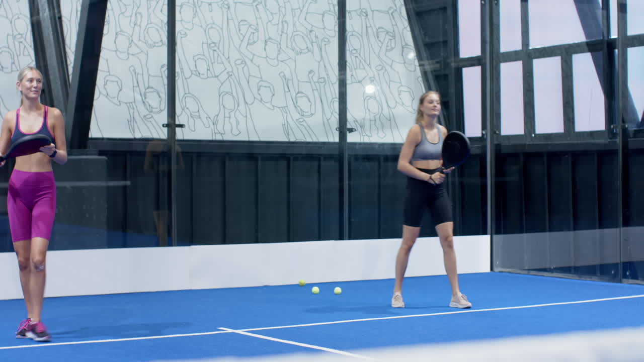 Women playing padel tennis on blue indoor court, focusing on game strategy