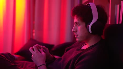 a concentrated man playing video games smiling with headphones looking at the tv screen light a little more cinematic