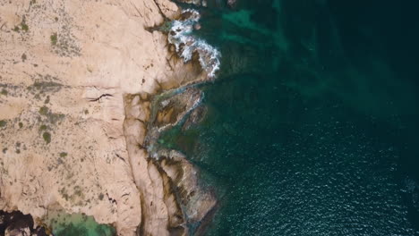 top down drone shot of waves crashing on coast of cliffs in cabo, mexico