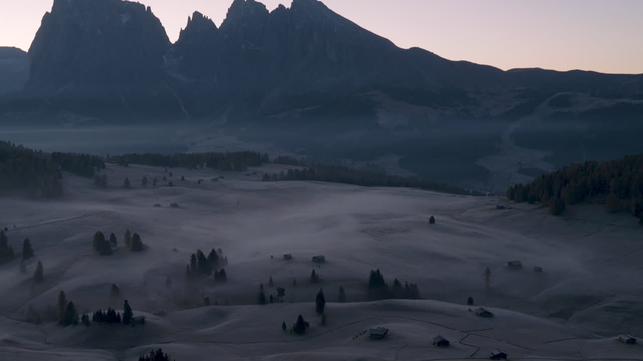 Cinematic aerial view of the Dolomites in Italy, rugged alpine peaks glowing at dawn, dramatic cliffs and deep shadowed valleys creating a serene high-altitude mood
