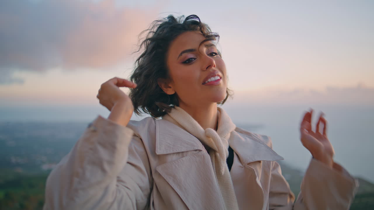 럭셔리 모델이 스카이라인을 포즈로 하고 곱슬머리를 조정하고 있습니다. 화려한 여성