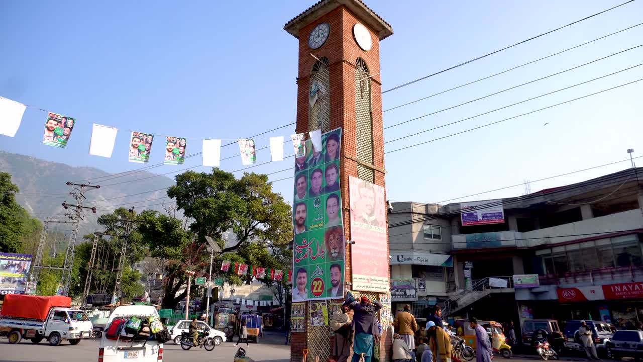 Muzaffarabad Chowk with election posters on a clock tower and local activity. Muzaffarabad, Azad Kashmir