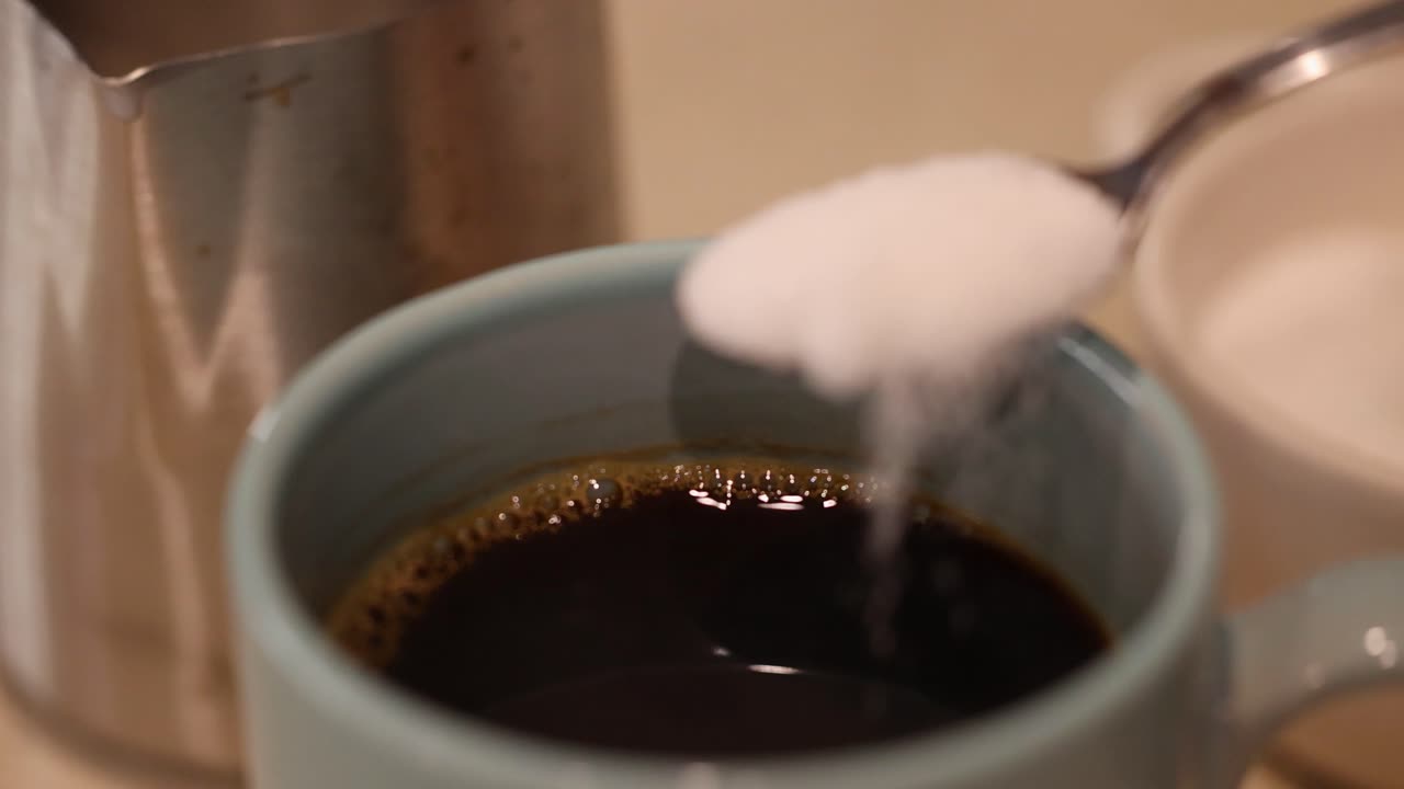 A spoonful of sugar is added to a steaming cup of coffee, enhancing its flavor