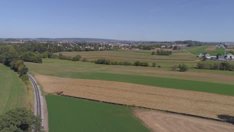 Luftaufnahme-Der-Amischen-Landschaft-Des-Landwirtschaftlichen-Arbeitsfeldes-An-Einer-Eisenbahnstrecke,-Während-Sich-Eine-Dampfmaschine-Nähert,-Wie-Sie-Von-Einer-Drohne-Gesehen-Wird