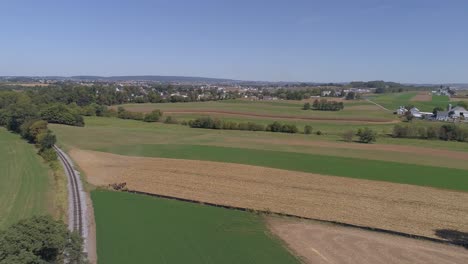 aerial view of amish countryside of farmer working field by a rail road track as a steam engine approaches as seen by a drone