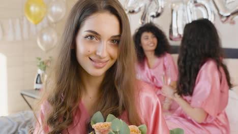 brunette woman holding bouquet, wearing pink silk nightdresses, smiling and looking at camera