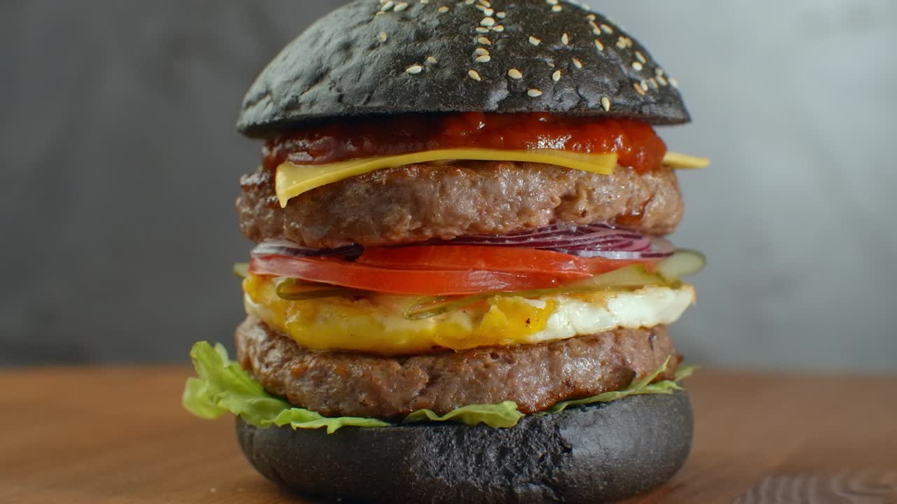 o hamburguesa con pan negro sobre un fondo borroso de hojas.