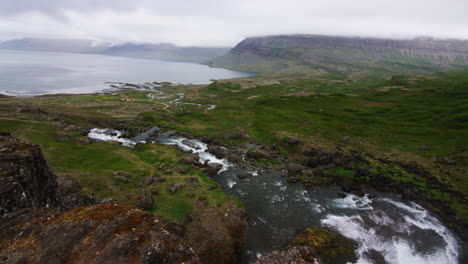 mountain river cascading downslope towards bay in fjord iceland, pan left