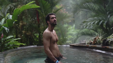 man in infinity pool in rain forest looks around at jungle, slow motion