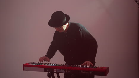 man in black outfit and hat plays red sampler against a vibrant pink backdrop, focused and artistic