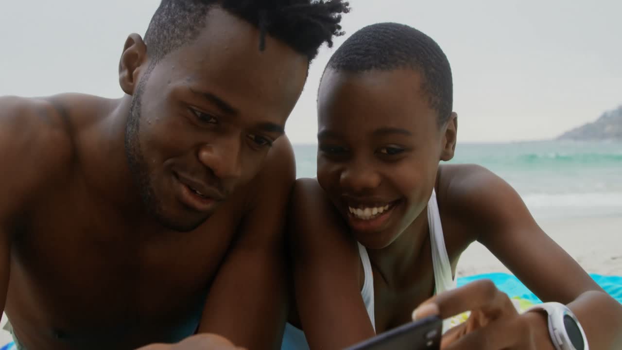 Front view of African american couple taking selfie with mobile phone on the beach 4k