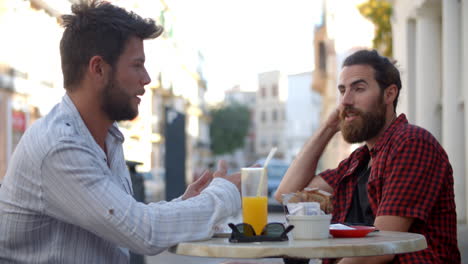 two male friends talking at a table outside a cafe, ibiza