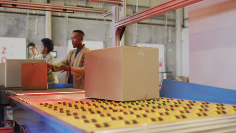 Diverse-male-and-female-workers-with-boxes-on-conveyor-belt-in-warehouse