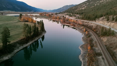 fiery embrace: thompson river bathed in sunset light as cars traverse british columbia's yellowhead highway