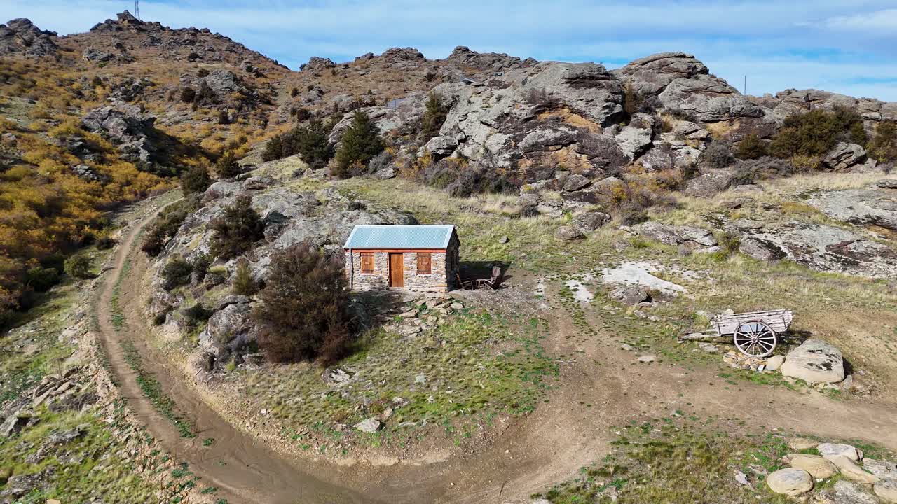 Aerial footage of a solitary cabin amidst rocky terrain and autumn foliage, captured by a drone in rural New Zealand