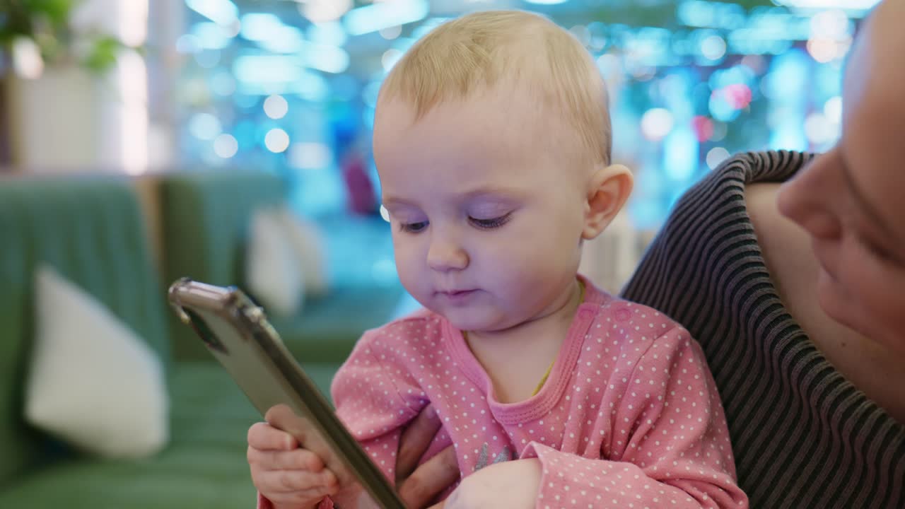 母親が見守る中、スマートフォンで遊ぶかわいい女の赤ちゃん
