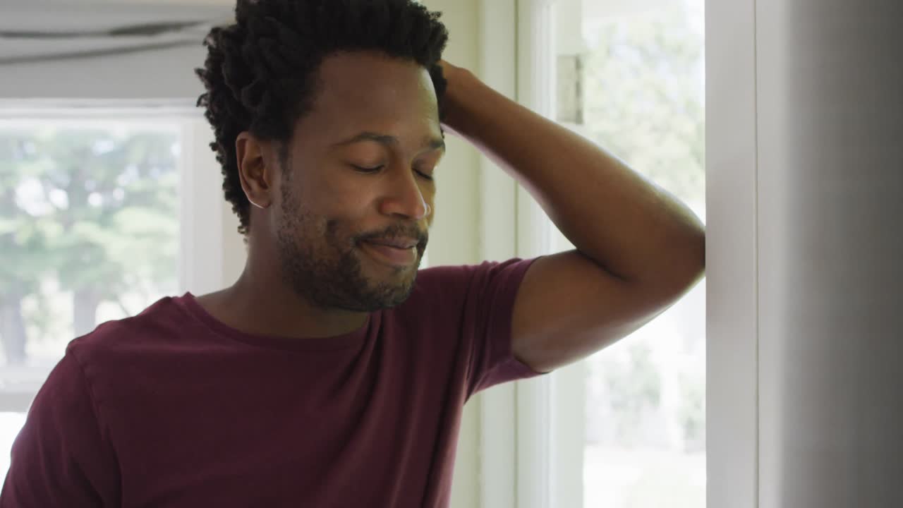retrato de un hombre biracial relajado de pie en la ventana con café y mirando a la distancia