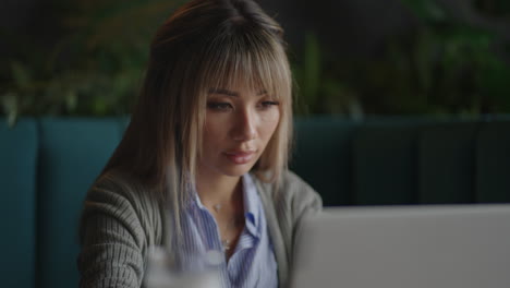 joven hermosa mujer de negocios asiática sonriente sosteniendo un café y una computadora portátil colocada en la mesa de madera en la oficina. mujer chequeando el correo o investigando mientras teletrabaja